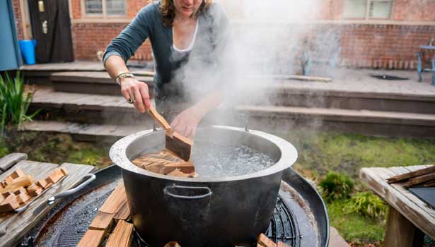 A person uses a brick to submerge wood chips in a pot of boiling water.