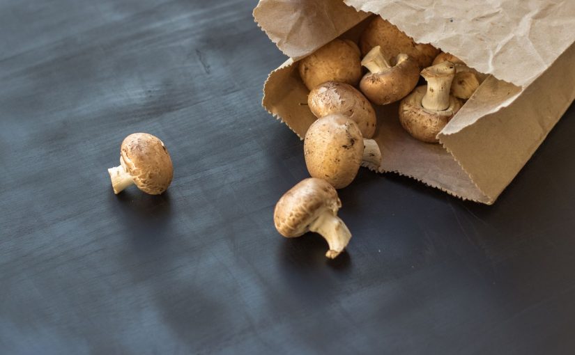 Paper bag with mushrooms spilling out on a dark surface, highlighting the best method for storing fresh mushrooms.