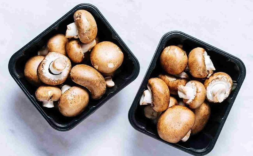 Two black plastic trays filled with fresh brown mushrooms, placed on a white marble surface.